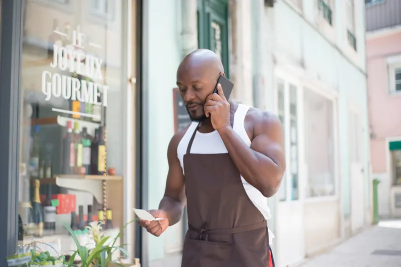 A business owner on a phone call with list in hand outside the restaurant